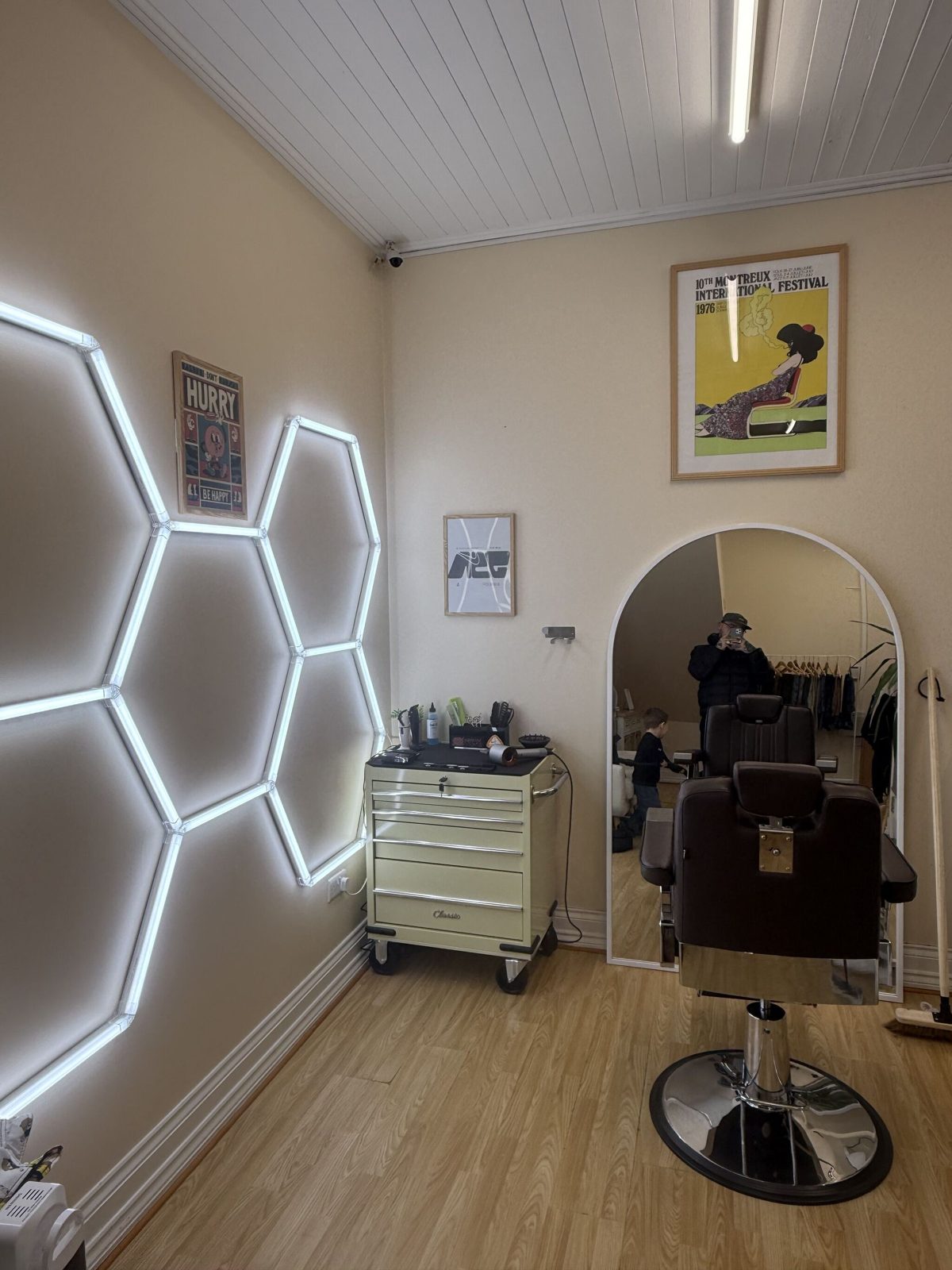 The barber chair in front of the arched mirror, with the hexagon light wall beside it