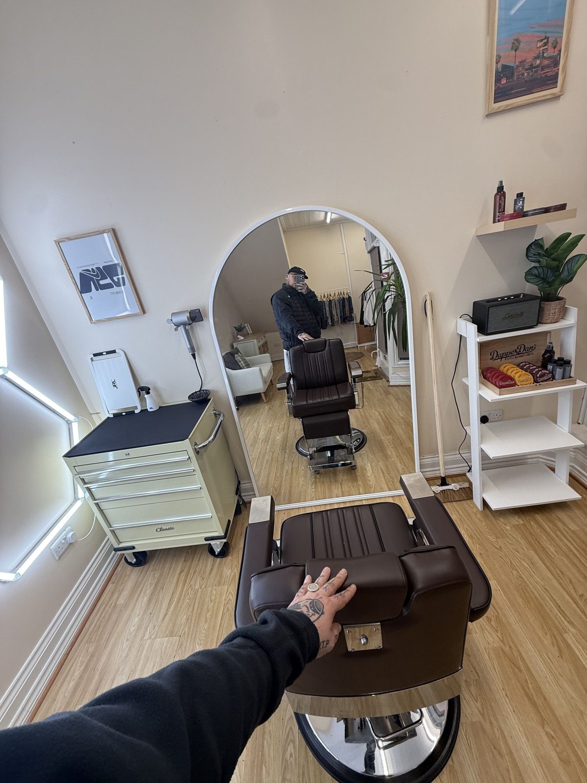 Two barber chairs, the cream tool trolley and a shelf of products